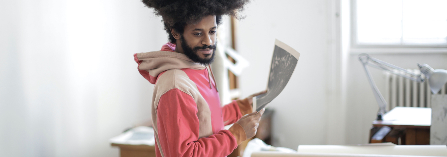 Man with afro wearing a sweatshirt in a studio holding up paper.